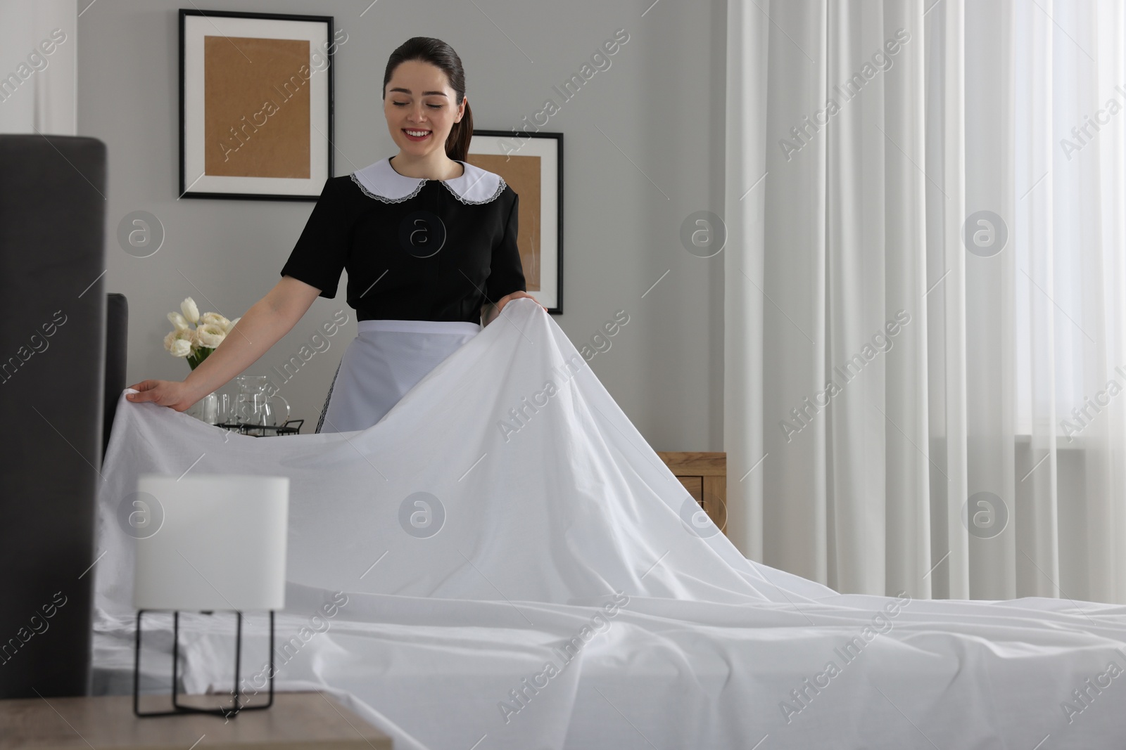 Photo of Young maid making bed in hotel room. Space for text