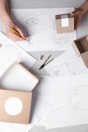 Photo of Man creating packaging design at light wooden table, top view