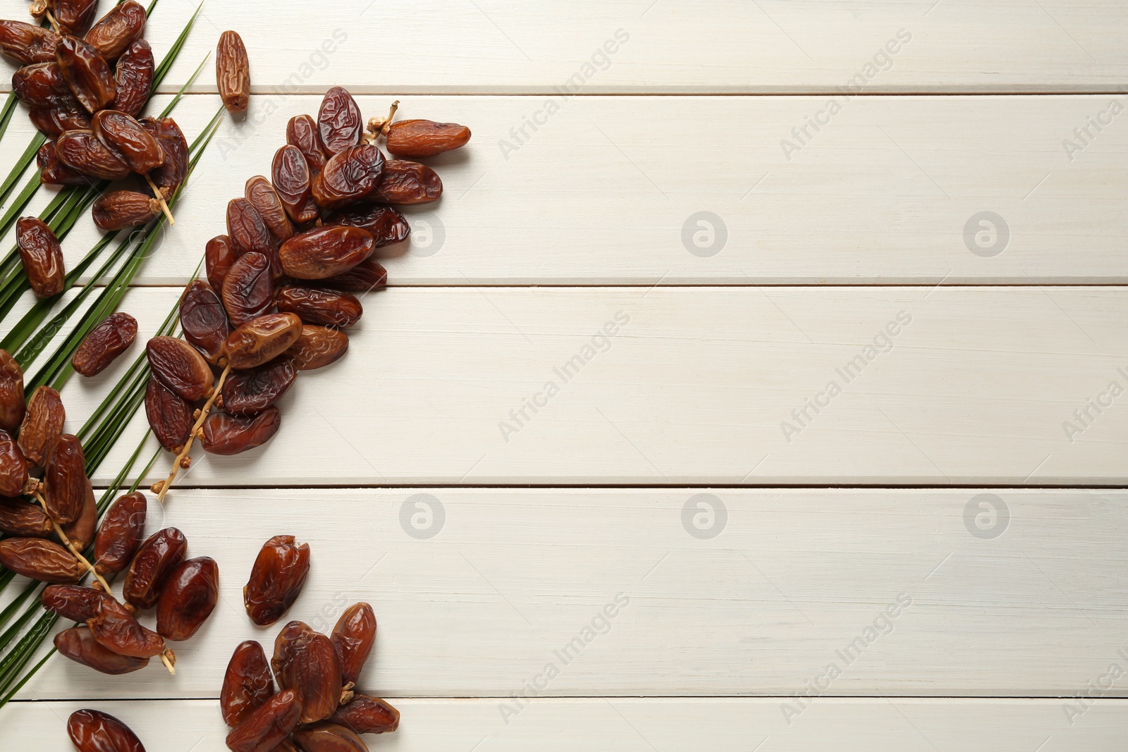 Photo of Tasty sweet dried dates with palm leaf on white wooden table, flat lay. Space for text