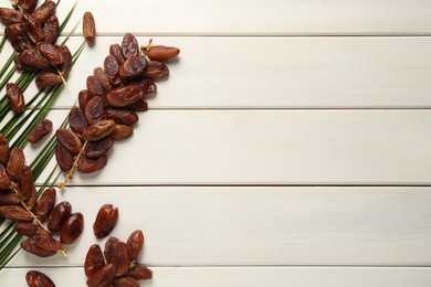 Photo of Tasty sweet dried dates with palm leaf on white wooden table, flat lay. Space for text