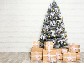 Photo of Decorated Christmas tree and gift boxes near white brick wall. Space for text