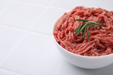 Photo of Fresh raw ground meat and rosemary in bowl on white tiled table, closeup. Space for text