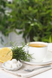 Aromatic herbal tea, fresh tarragon sprigs, sugar cubes and lemon on white table, space for text