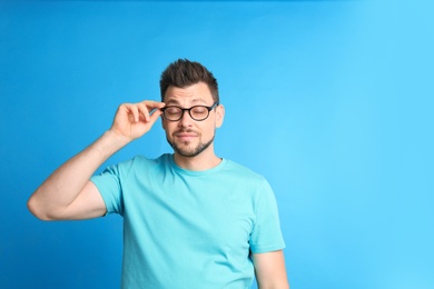 Photo of Man with vision problems wearing glasses on blue background, space for text
