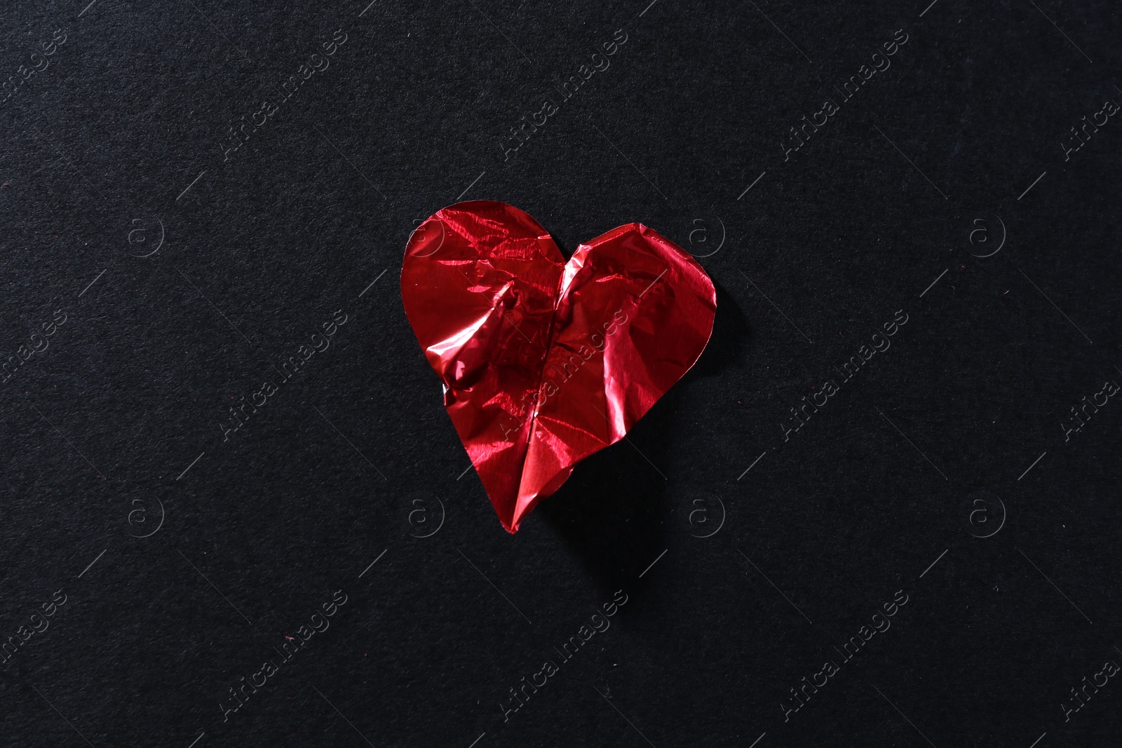 Photo of Red crumpled paper heart on black background, top view. Breakup concept