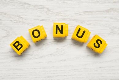 Image of Word Bonus made of yellow cubes with letters on white wooden background, top view