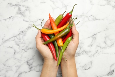 Photo of Young woman with handful of different hot chili peppers at marble table, top view
