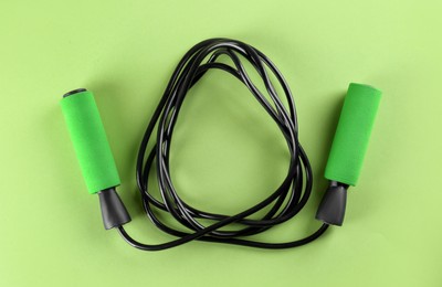 Photo of Skipping rope on light green background, top view. Sports equipment