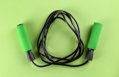 Skipping rope on light green background, top view. Sports equipment