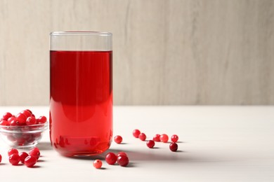 Photo of Tasty cranberry juice in glass and fresh berries on white wooden table, closeup. Space for text