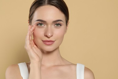 Photo of Young woman applying cream under eyes on beige background, space for text