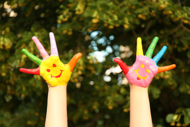 Photo of Kid with smiling face drawn on palms in green park, closeup. School holidays