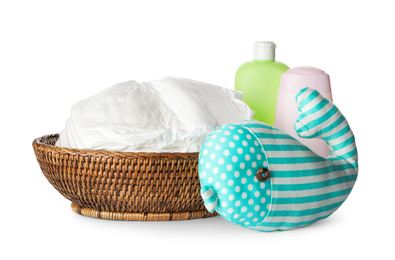 Photo of Wicker bowl with disposable diapers, toy and toiletries on white background