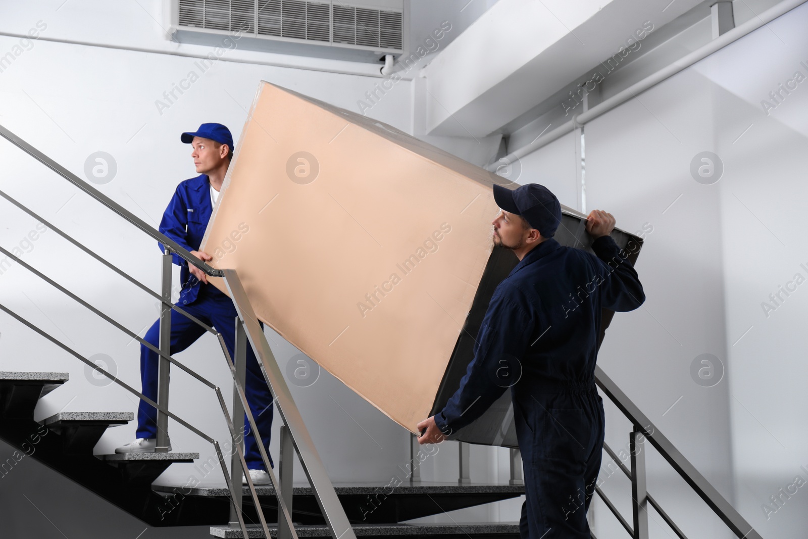 Photo of Professional workers carrying refrigerator on stairs indoors