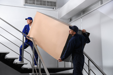 Photo of Professional workers carrying refrigerator on stairs indoors