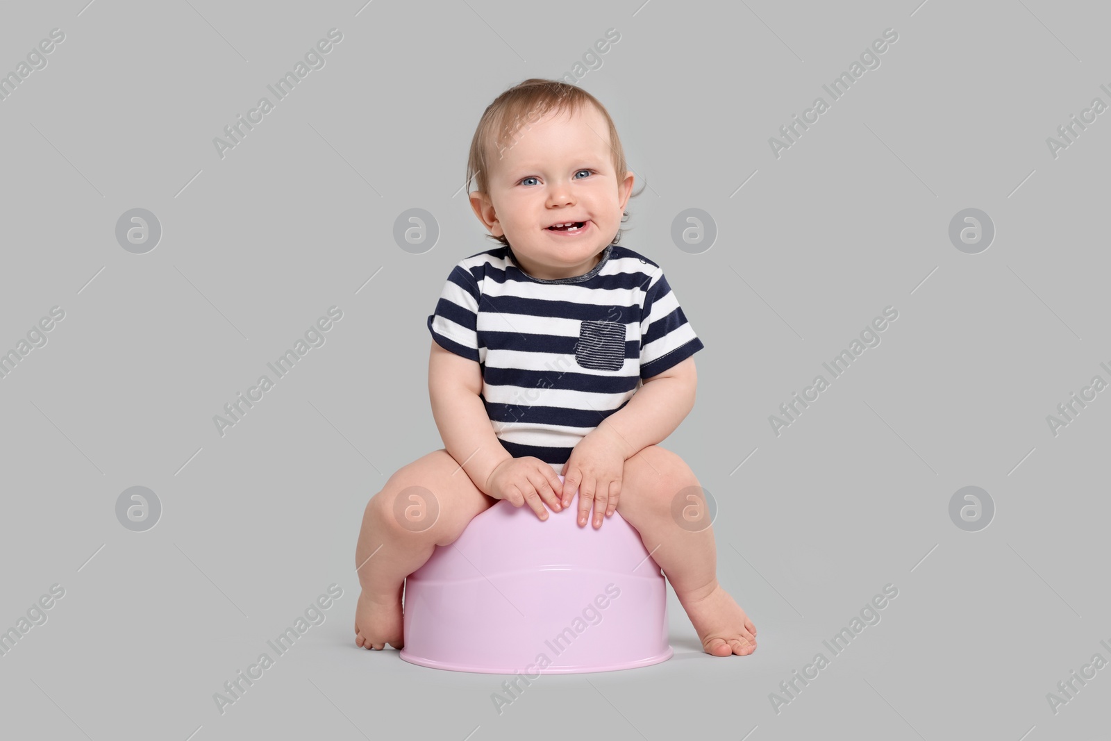 Photo of Little child sitting on baby potty against light grey background