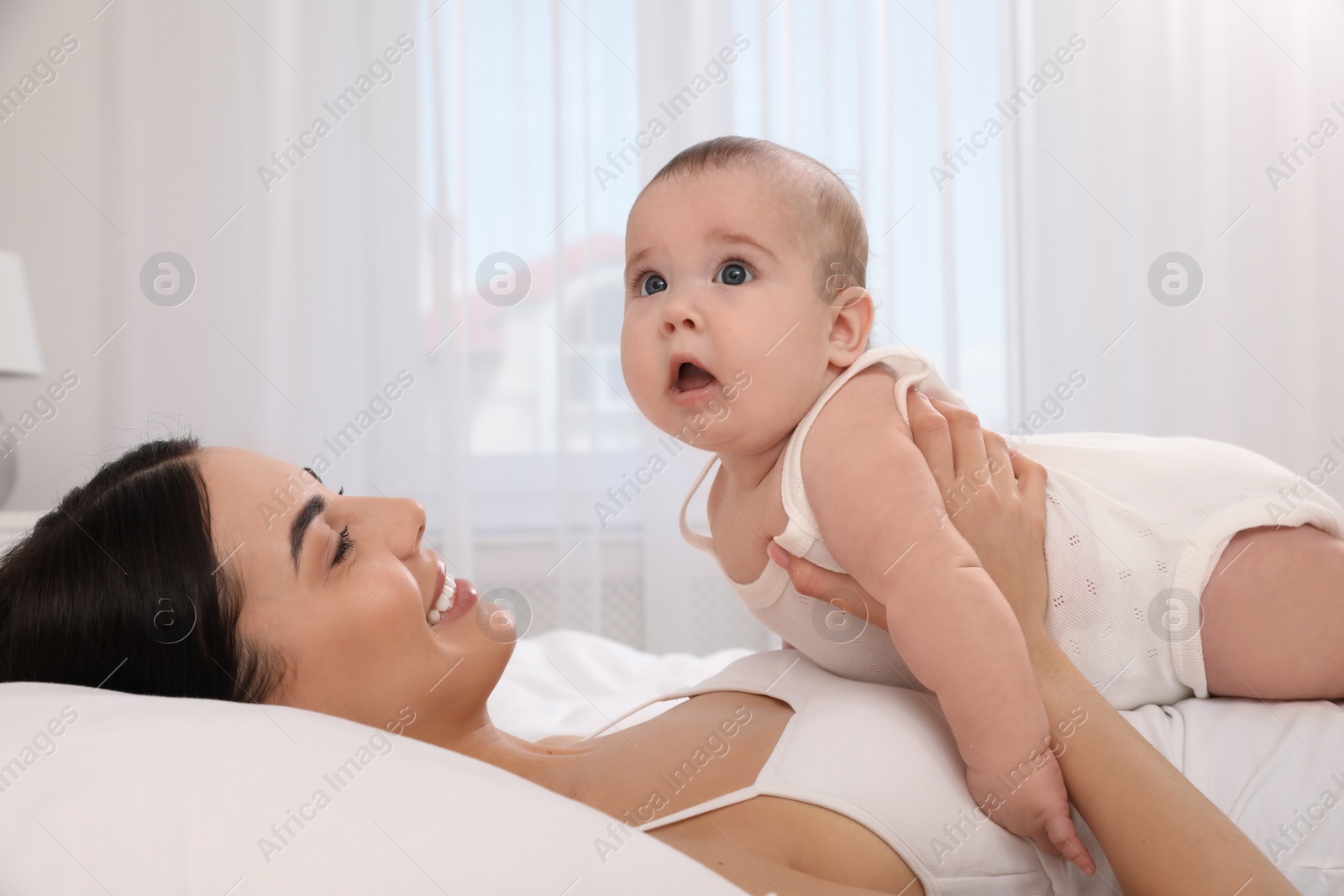 Photo of Young mother with her little baby on bed at home