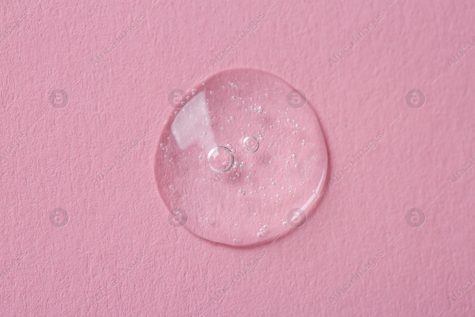 Photo of Drop of cosmetic serum on pink background, top view