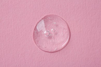 Photo of Drop of cosmetic serum on pink background, top view
