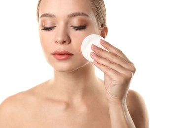 Portrait of beautiful young woman removing makeup with cotton pad on white background