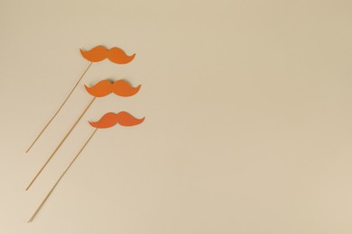 Fake paper mustaches party props on beige background, flat lay. Space for text