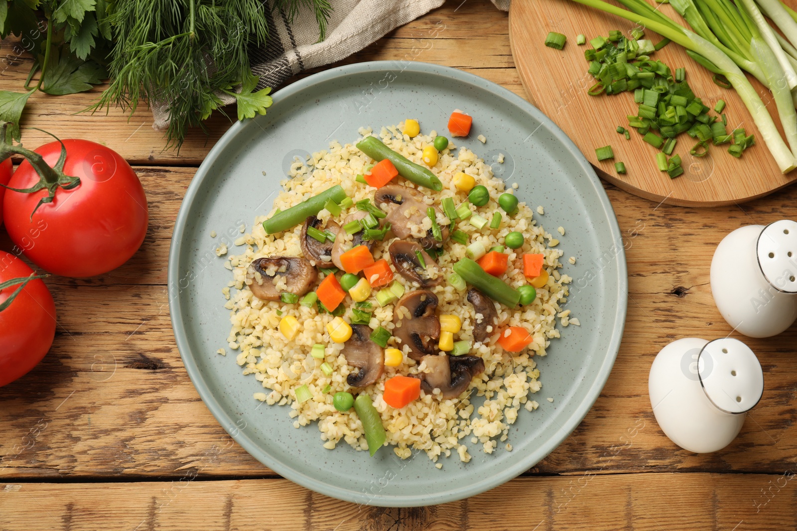 Photo of Delicious bulgur with vegetables and mushrooms served on wooden table, flat lay