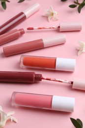 Different lip glosses, applicators, flowers and green leaves on pink background