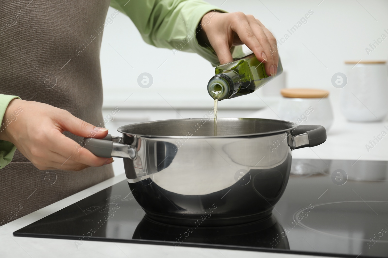 Photo of Woman pouring cooking oil from bottle into pot in kitchen, closeup