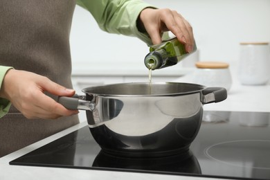 Photo of Woman pouring cooking oil from bottle into pot in kitchen, closeup