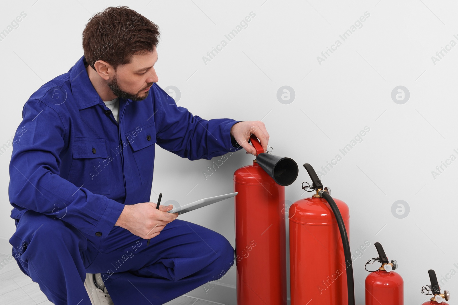 Photo of Man with tablet checking fire extinguishers indoors