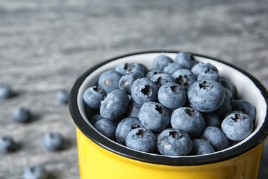 Photo of Fresh blueberries in yellow cup on color table, closeup