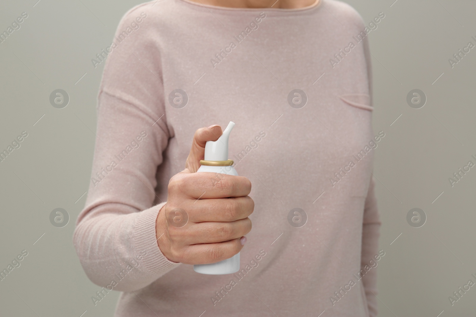 Photo of Woman holding nasal spray against light grey background, closeup