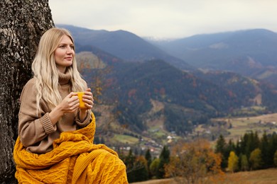 Young woman with mug of hot drink in mountains. Space for text