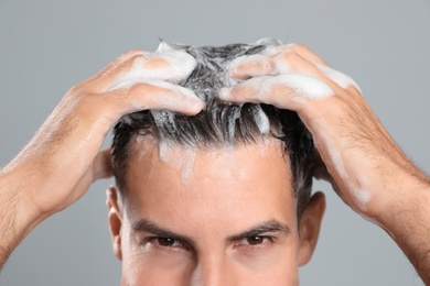Handsome man washing hair on grey background, closeup