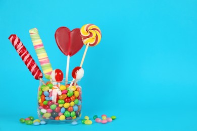 Glass jar with different candies on light blue background, space for text