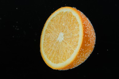 Photo of Half of orange in sparkling water on black background. Citrus soda