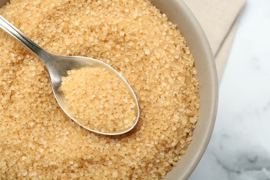 Brown sugar in bowl and spoon on white table, top view