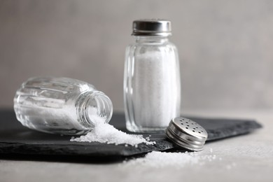 Photo of Natural salt in shakers on grey table, closeup