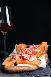 Photo of Wooden board with melon, prosciutto and blueberries on table against black background