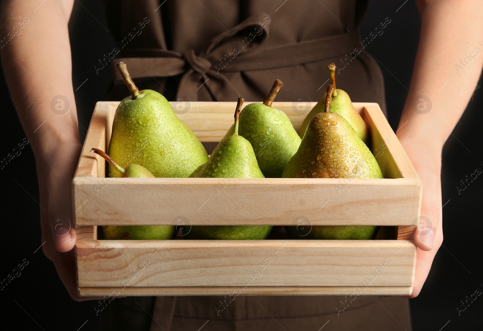 Photo of Woman holding wooden crate with ripe pears on black background, closeup