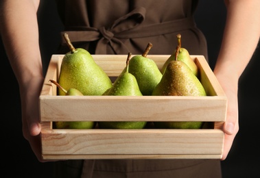 Woman holding wooden crate with ripe pears on black background, closeup