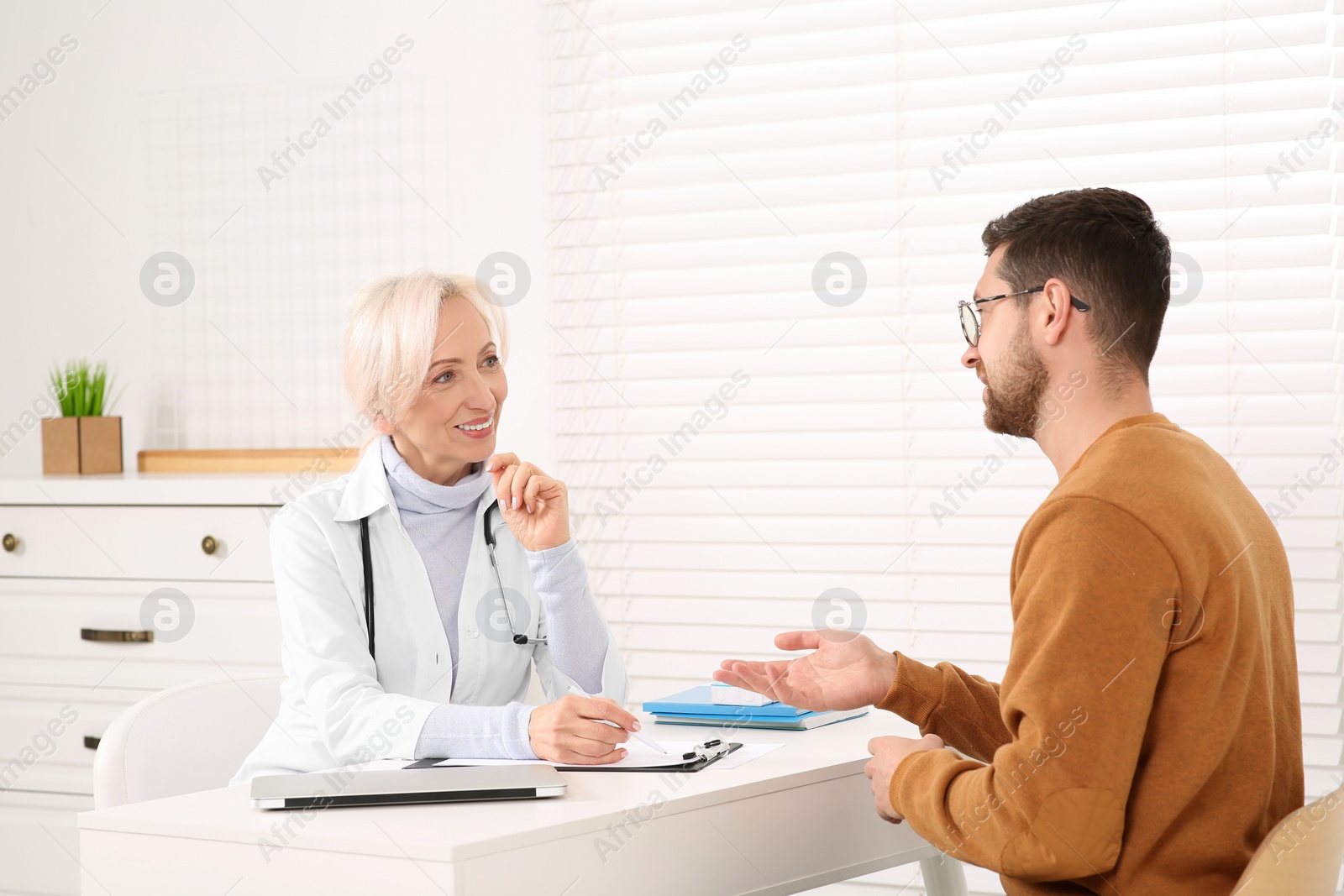 Photo of Doctor consulting patient at white table in clinic