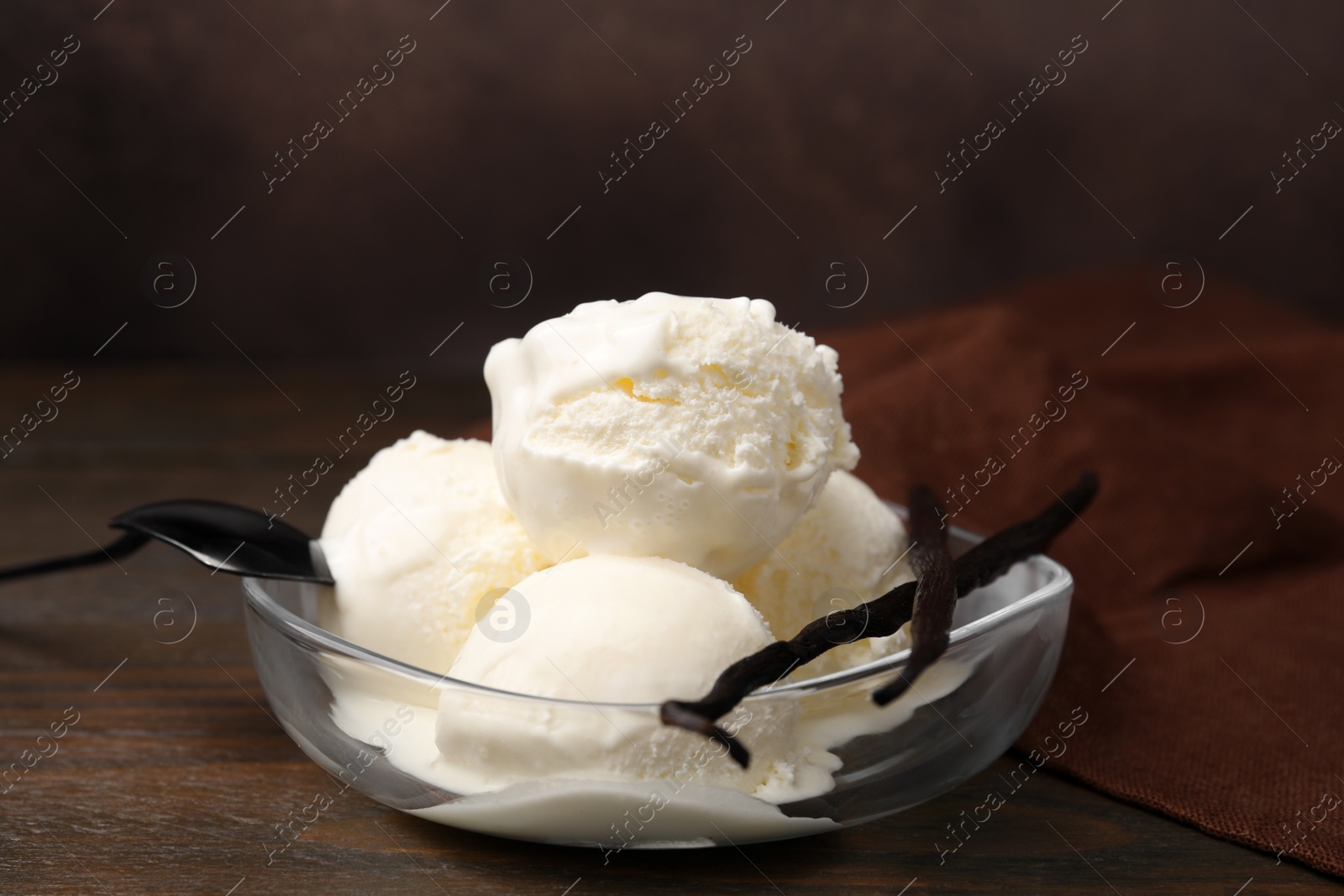 Photo of Delicious ice cream and vanilla pods in bowl on wooden table, closeup