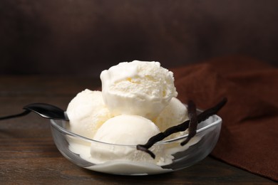 Photo of Delicious ice cream and vanilla pods in bowl on wooden table, closeup