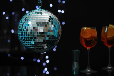 Photo of Shiny disco ball hanging over bar counter with cocktails in nightclub, space for text
