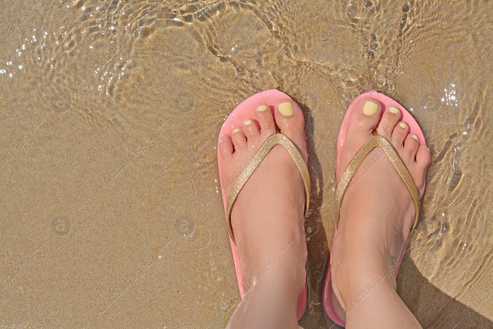 Photo of Woman wearing stylish pink flip flops standing in shallow sea water, top view. Space for text