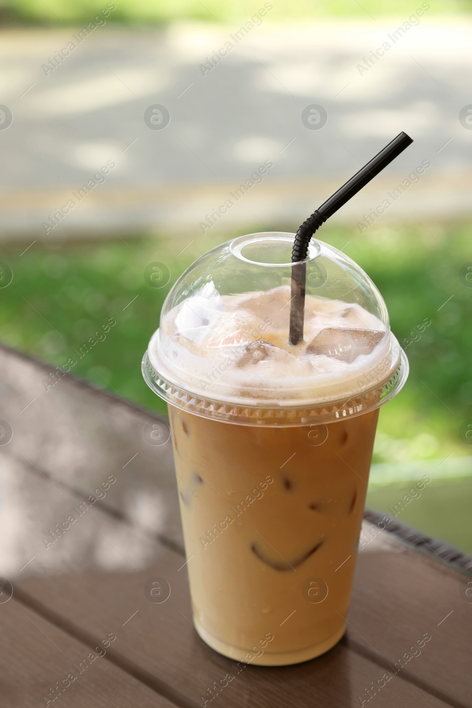 Photo of Plastic takeaway cup of delicious iced coffee at table in outdoor cafe
