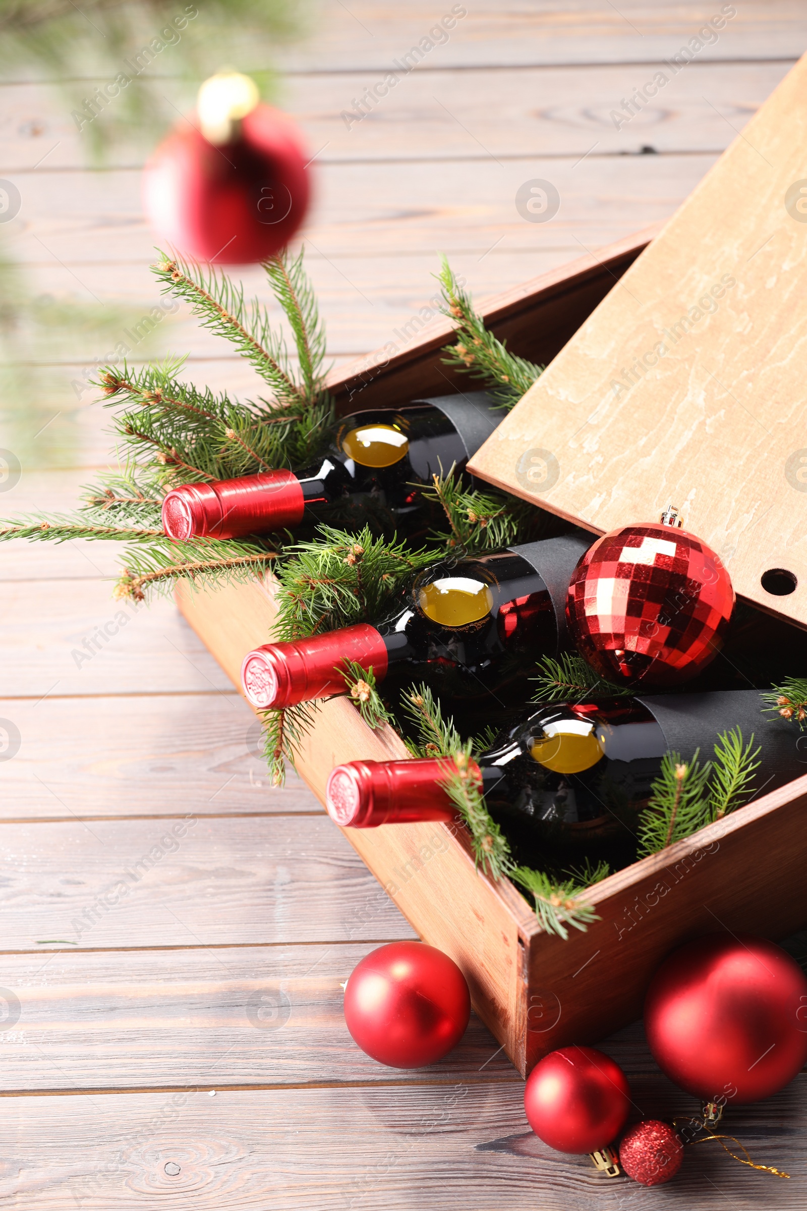 Photo of Wooden crate with bottles of wine, fir twigs and red Christmas balls on table