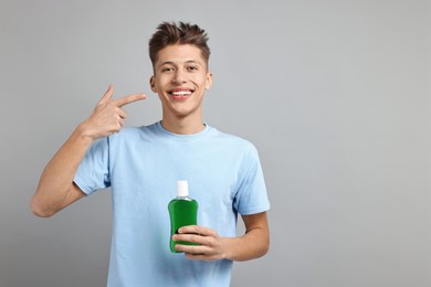 Young man with mouthwash pointing at his healthy teeth on light grey background, space for text