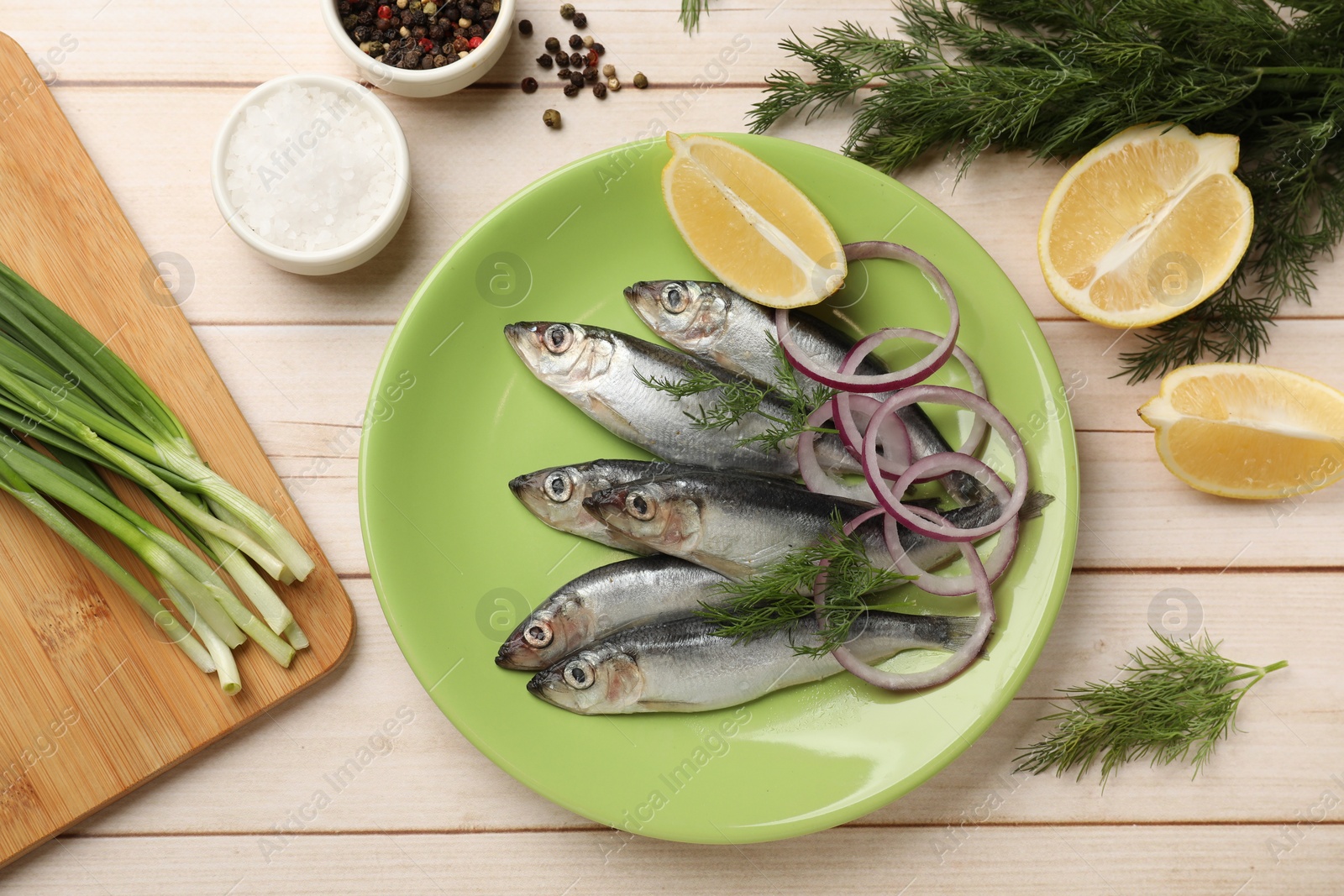 Photo of Fresh raw sprats, cut lemon, onion, dill and spices on light wooden table, flat lay